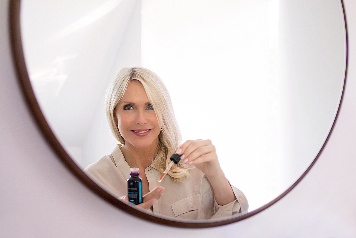 Woman in a mirror holding SkinCeuticals Hyaloronic Acid from SkinCeuticals blog post on Lifetime-Pieces.com