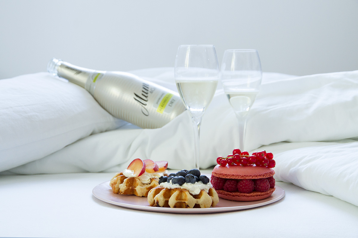 breakfast in bed plates waffles with cream cheese and fruits macaron two glasses bottle of champagne white linen