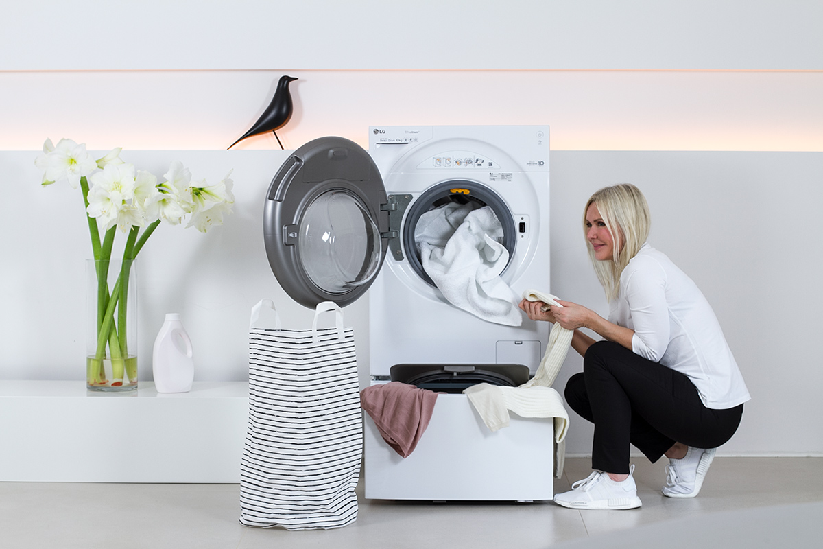 women in squatting positions beside a washer, washing machine, laundry, folded, white flowers, liquid laundry detergent bottle, white flowers, picture from LG TwinWash blog post on lifetime-pieces.com