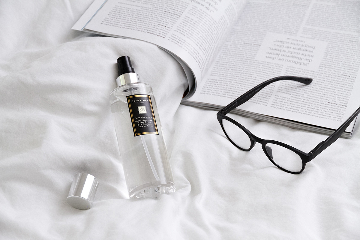 Jo Malone London, living in a scented home, linen spray, black glasses, open magazine on a bed with white linen
