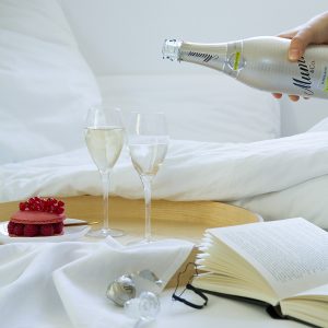 breakfast in bed hand holding a bottle filling two glasses of champagne macarons