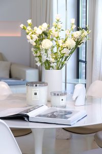 Jo Malone London, living in a scented home, white Saarinen table with Tulip chairs, scented candles, a vase with white spring flowers and a coffee table book on the table