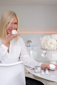 blonde woman sitting on a chair, table, holding Neutrogena cellular boost skincare product in her hand
